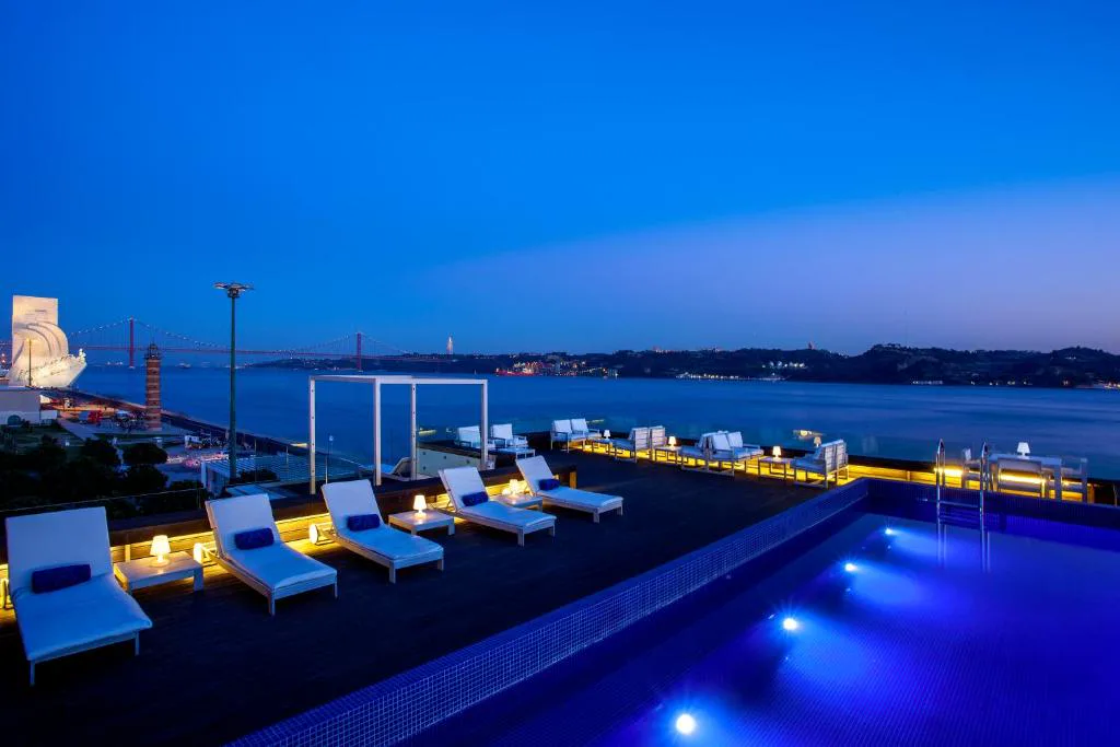 Piscina en la azotea de Altis Belém Hotel & Spa al anochecer, con el Padrão dos Descobrimentos y el puente 25 de Abril al fondo