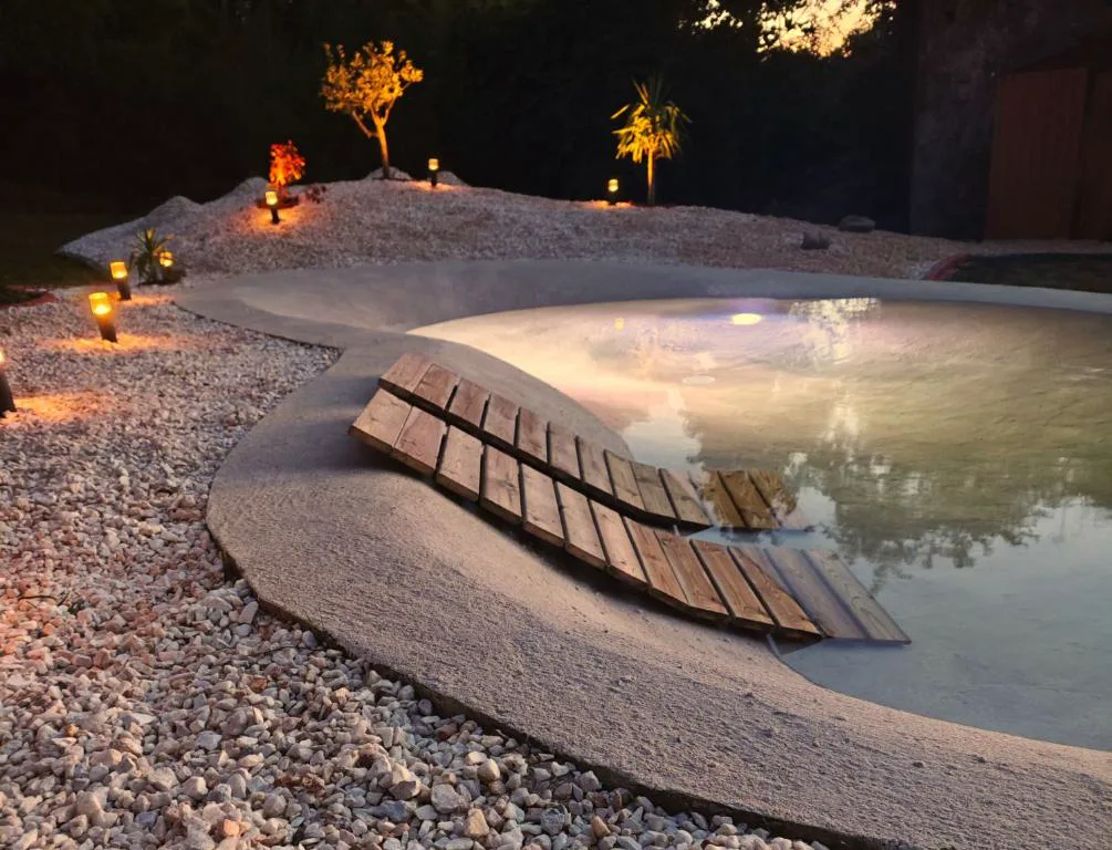 Piscina de formas orgánicas iluminada al atardecer con pasarela de madera, As Alvarizas, Moraña