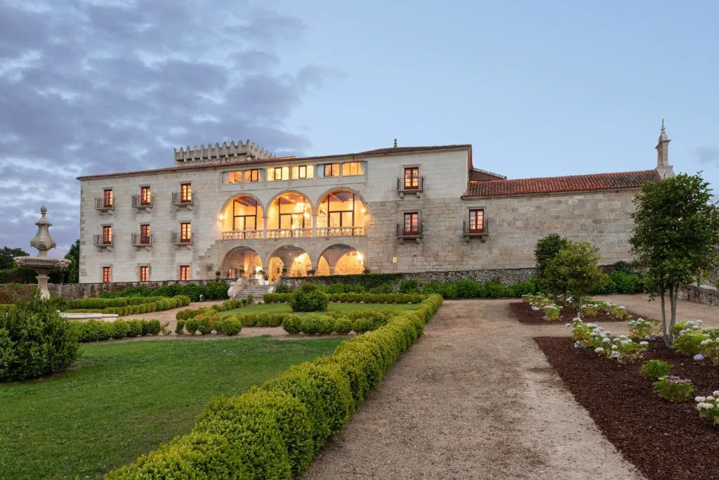 Fachada renacentista del Áurea Palacio de Sober iluminada al atardecer, con jardines y fuente de piedra