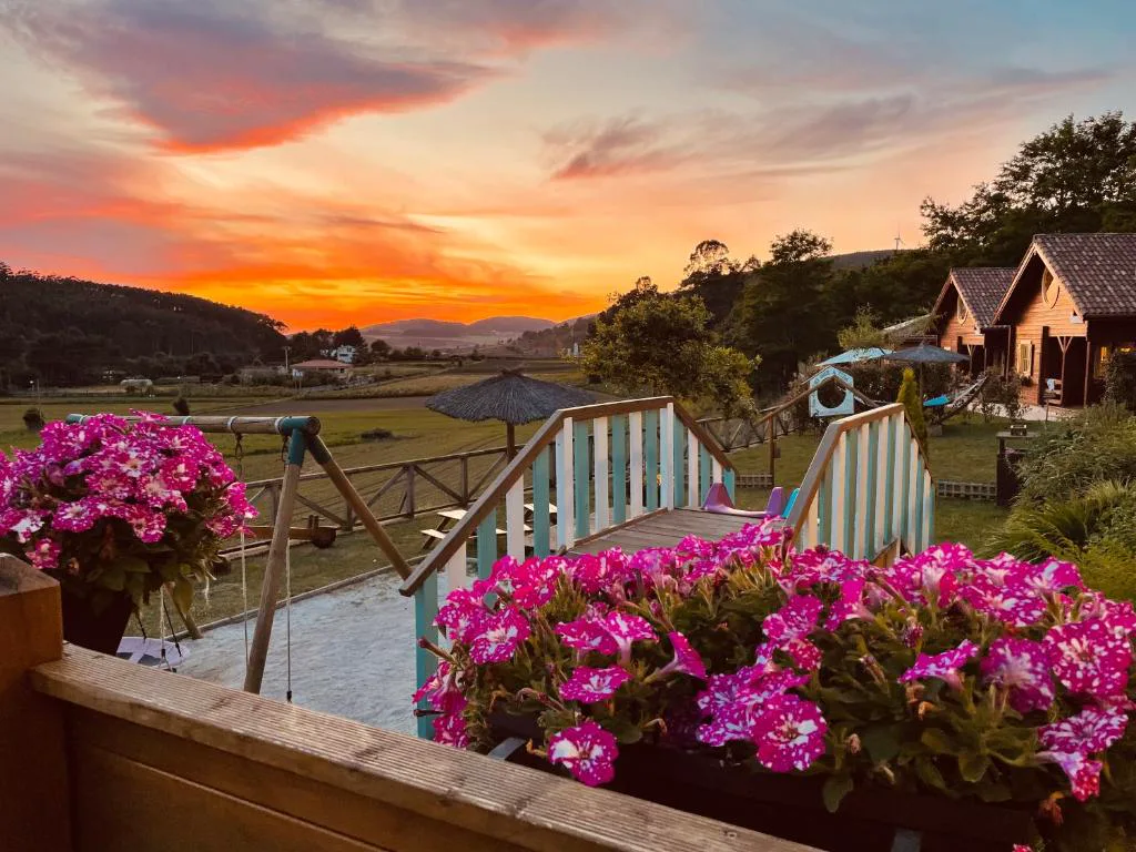 Puesta de sol naranja sobre las cabañas de madera y el valle, Cabanas da Ría, Lires