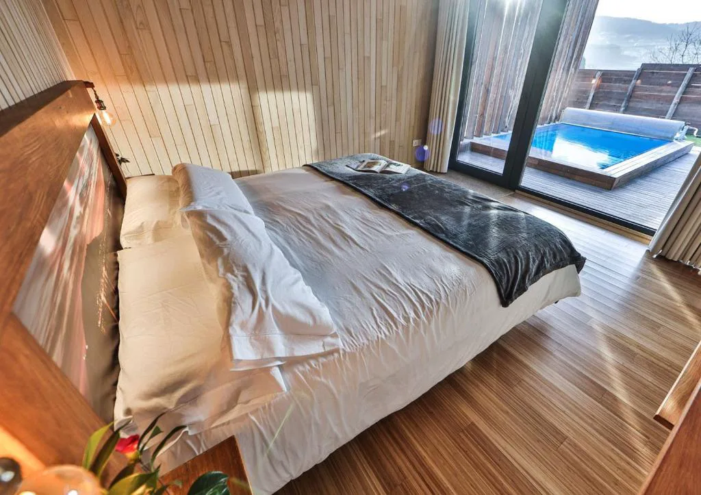 Dormitorio con vistas directas a la piscina privada y al valle al atardecer, Cabañas de Mallas, Fisterra