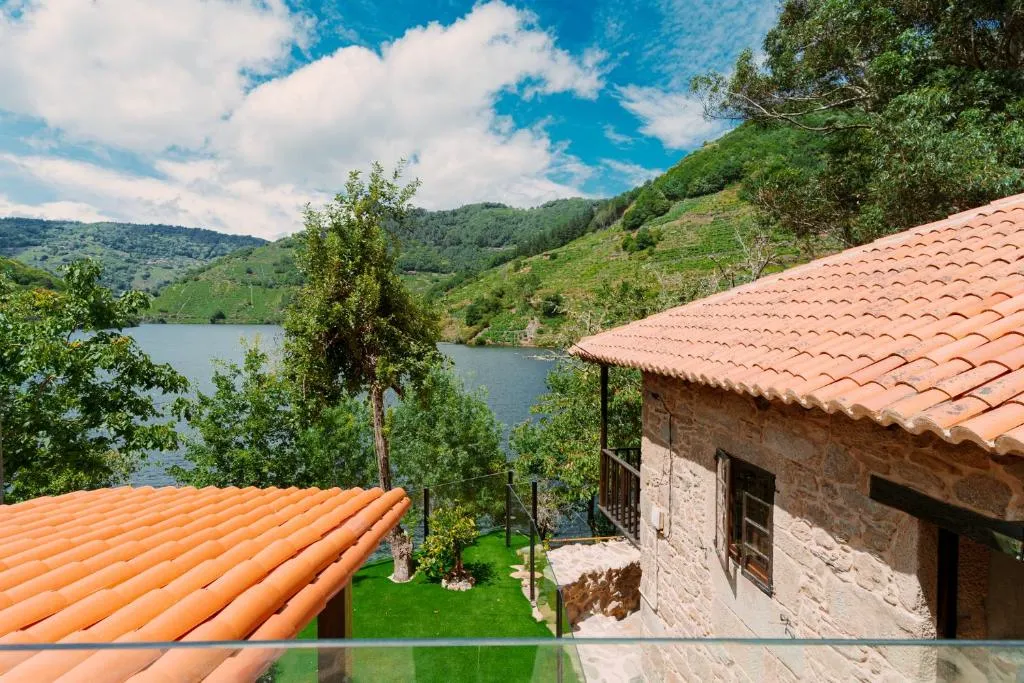 Casa de piedra con tejado a dos aguas frente al río Miño, entre viñedos en terrazas de la Ribeira Sacra, en Chantada