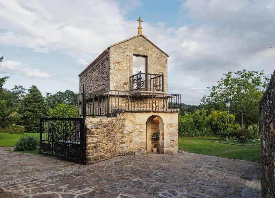Antiguo hórreo de piedra restaurado con balcón y cruz en la cima, Hórreo Lar San Adrián, Coristanco