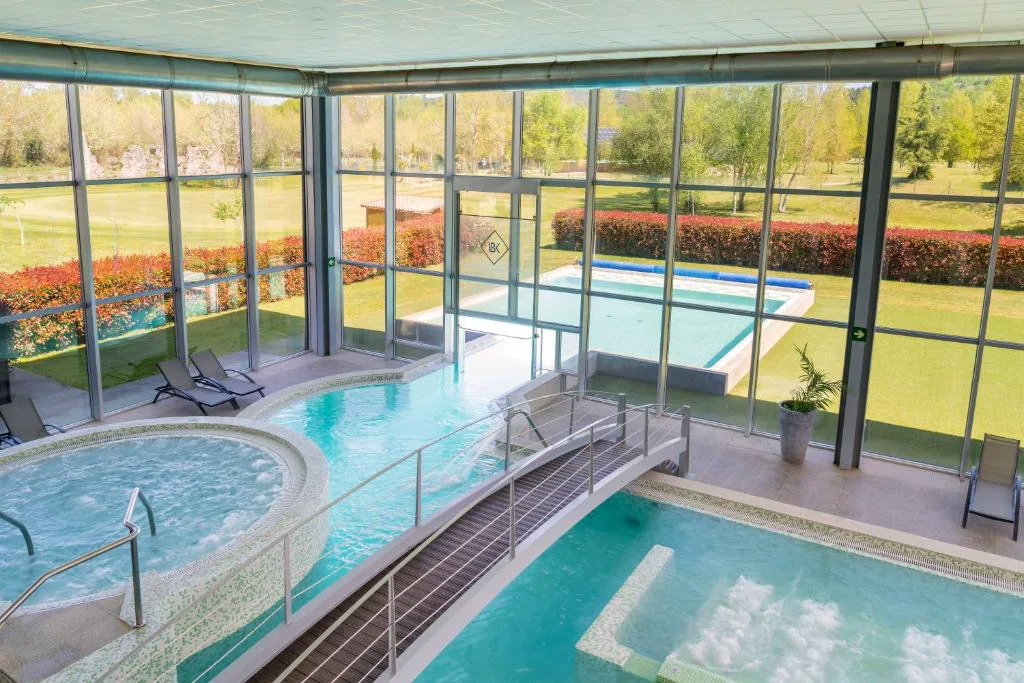 Circuito termal interior con jacuzzi, piscina y puente de madera sobre el agua, con vistas al campo de golf, IBERIK Augas Santas