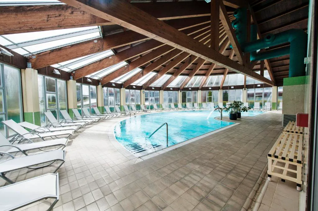 Piscina interior climatizada bajo techo de madera con grandes ventanales, Lobios Caldaria Hotel Balneario