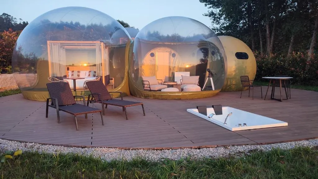 Burbujas transparentes de Luzada Glamping al atardecer, con jacuzzi exterior en la costa de Xove, Lugo